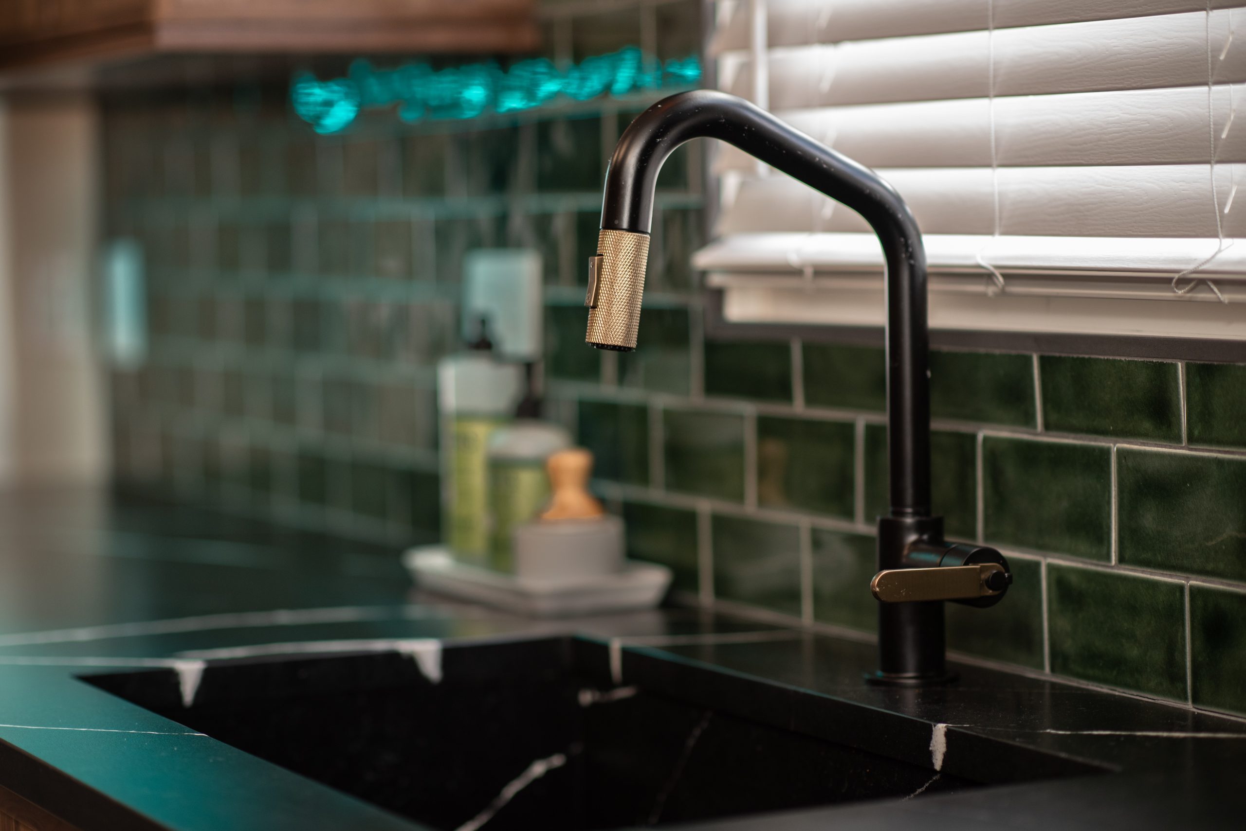 A modern kitchen with bold colors, featuring a green tile backsplash and a dark counter-cutout sink with black and gold accents.