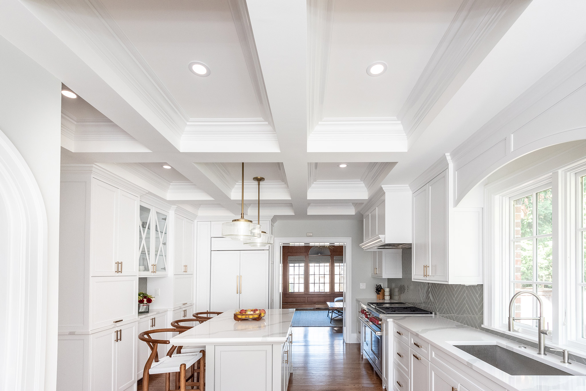 A bright and classic kitchen design with a modern twist, featuring white cabinets, a gray tile backsplash, and a coffered ceiling.