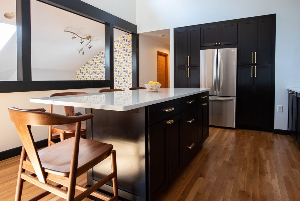 A modern kitchen interior with bold black and white contrasts and a classic hardwood floor.