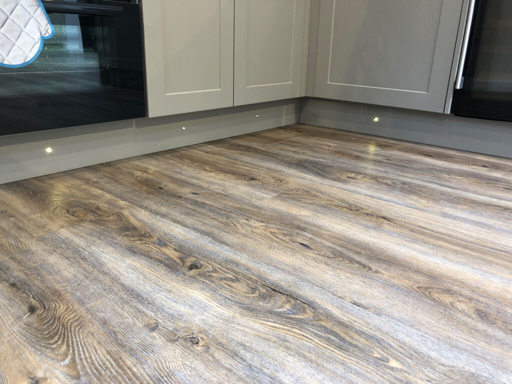 Image of spot halogen lights under grey kitchen cabinets / cupboards, floor lighting in interior design of under cabinet LED lighting kit and kitchen plinth lights on kickboards for illumination of oak wooden floorboards vinyl flooring by cooker stove